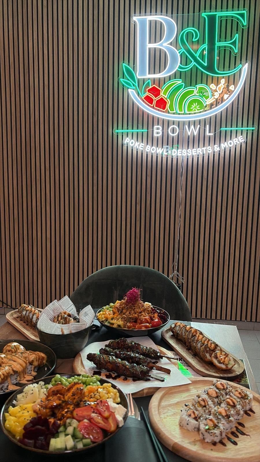 Tafel vol bowls, sushi en yakitori onder het B&F Bowl-neonbord